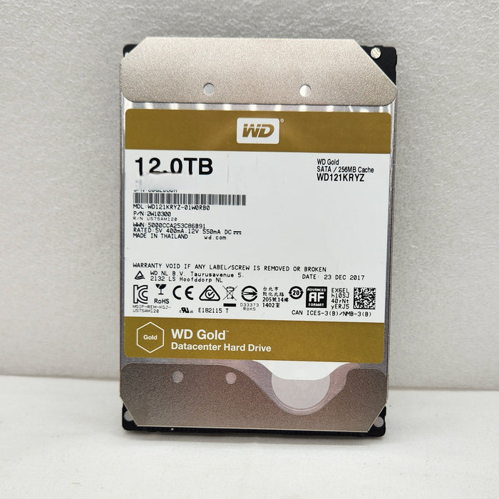 A Western Digital 12.0TB WD Gold internal hard drive, model WD100XBXZ, standing upright against a light gray textured wall.
